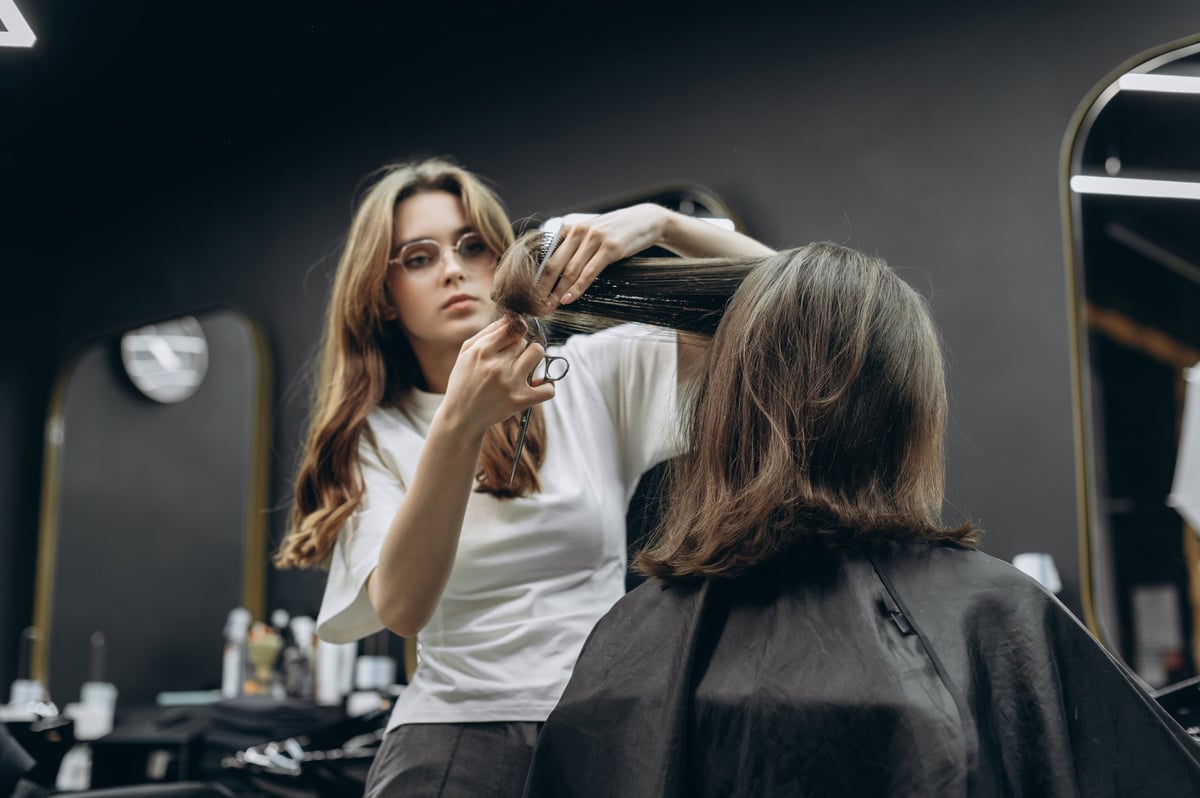 Stylist cutting a client's long hair with scissors in a modern salon